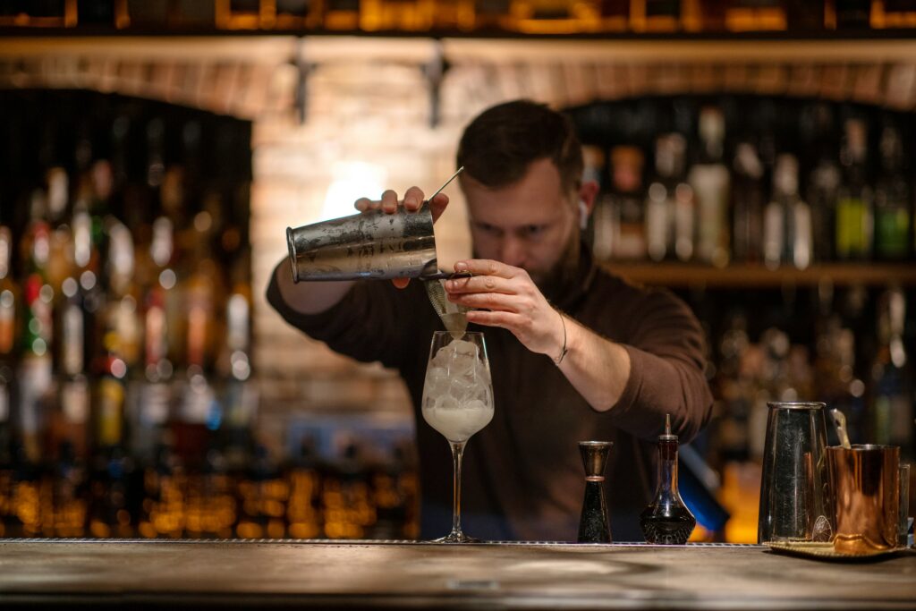 Barkeeper schüttet Getränk aus Mischbecher in Glas.